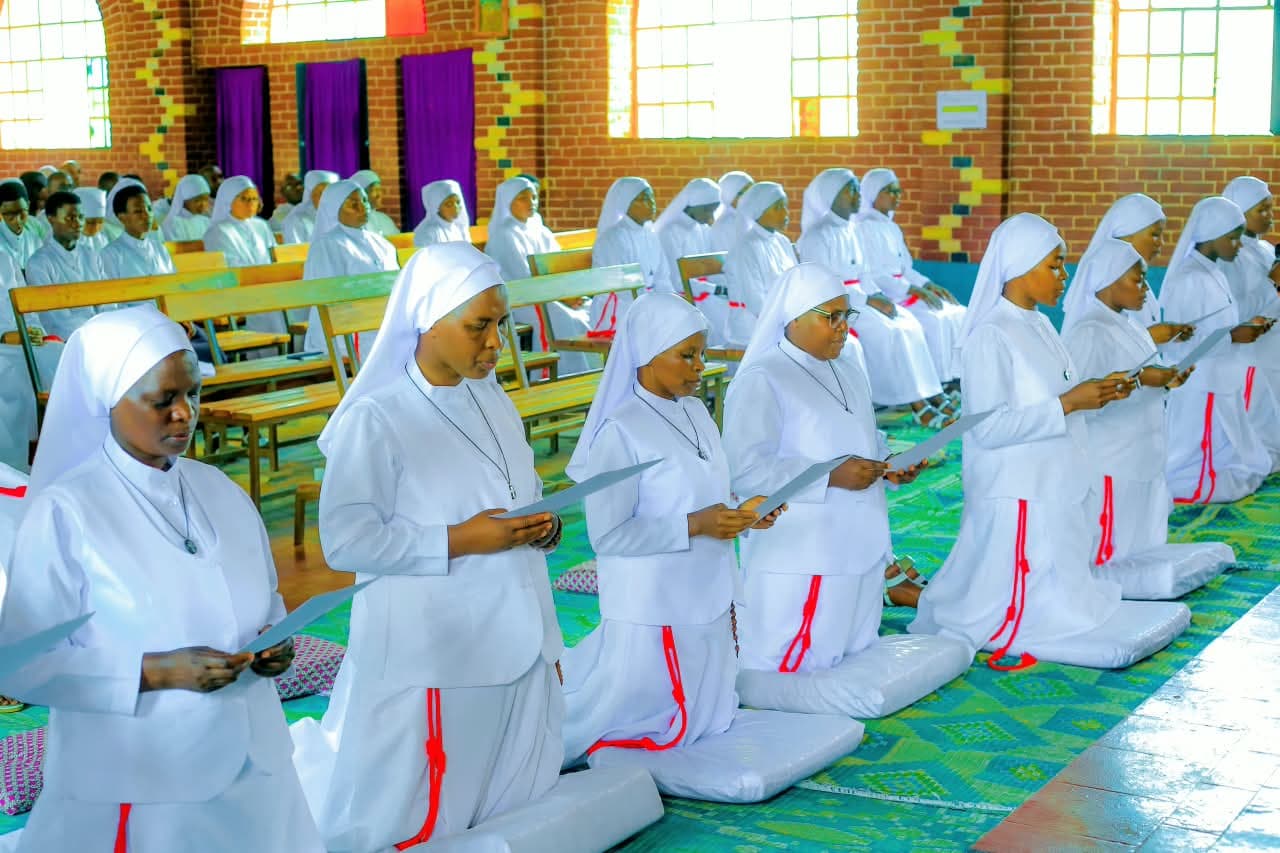 Sœurs MPC agenouillées en habit blanc, lisant leurs vœux, dans une église en briques baignée de lumière